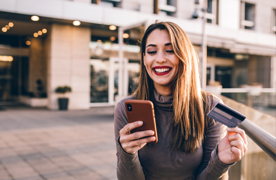 Young woman looking at phone with credit card in hand